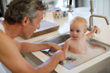 Obraz na płótnie Canvas Father bathing baby in kitchen sink