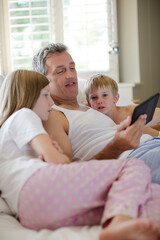 Obraz premium Father and children using digital tablet on bed