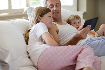 Obraz premium Father and children using digital tablet on bed