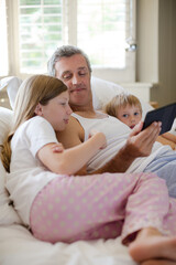 Obraz premium Father and children using digital tablet on bed