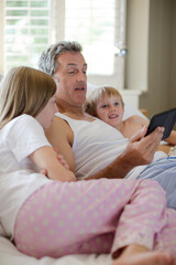 Obraz premium Father and children using digital tablet on bed