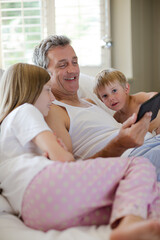 Obraz premium Father and children using digital tablet on bed