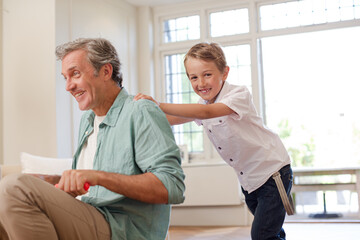 Boy pushing father on tricycle indoors