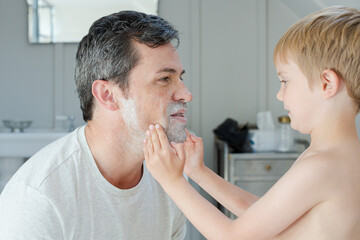 Boy rubbing shaving cream on father's face