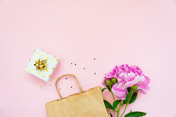 Flat lay of shopping bag, gift box and peony flower over pink background. Copy space.