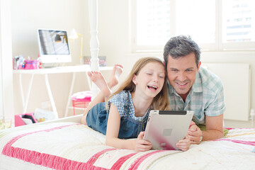 Father and daughter using digital tablet on bed