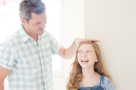 Father measuring daughter's height on wall