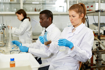 Focused women lab technicians in glasses working with reagents and test tubes, man on background