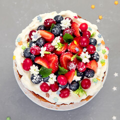 Delicious homemade cake with fresh berries and mascarpone cream on gray background.
