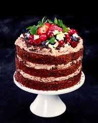 Delicious homemade chocolate cake with fresh berries and mascarpone cream on dark background.