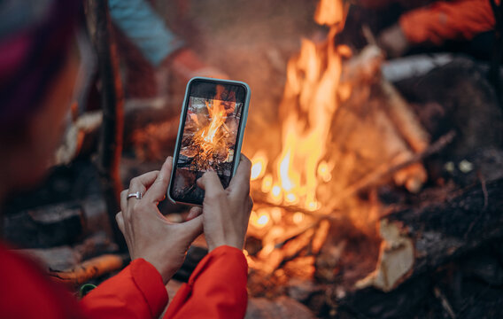 man with a watch on his hands takes pictures on a modern mobile phone of a burning bonfire in nature. Photo in smartphone photos. The concept of accessible photography.