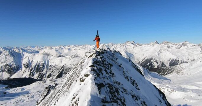 Young male mountaineer climbing a peak with skis in winter with lots of fresh snow. Mountain guide climbing extreme mountain ridge on a cold winter day with awesome alpine mountain landscape tyrol.