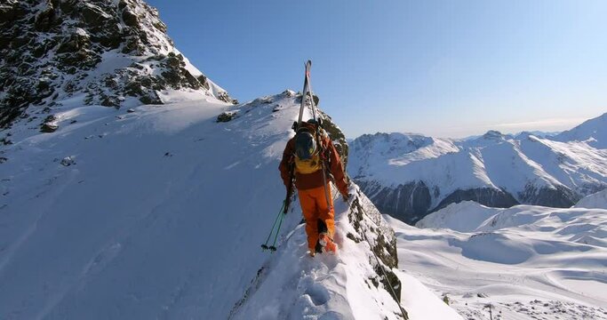 Mountain climber hiking in deep snow on a ridge at a mountain peak. Extreme mountaineering in winter with skis in wonderful winter alpine landscape and lots of fresh snow. Tyrolean mountaineering 4K