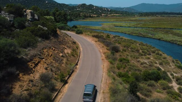 Aerial follow of VW T4 Volkswagen Bulli hippie van car is driving along a road at the seaside coast of the island Sardinia in Italy with the blue sea. Van life wild camping freedom tourism vacation.