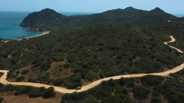 VW T4 Volkswagen Bulli hippie van car is driving along a road at the seaside coast of the island Sardinia in Italy with the blue sea and horizon. Van life wild camping freedom tourism vacation aerial.
