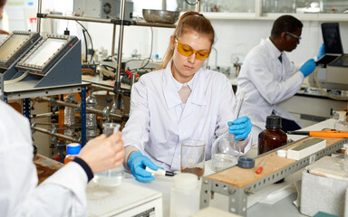 Fototapeta na wymiar Focused woman lab technicians in glasses working with reagents and test tubes, man on background