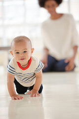 Mother watching baby boy crawl in living room