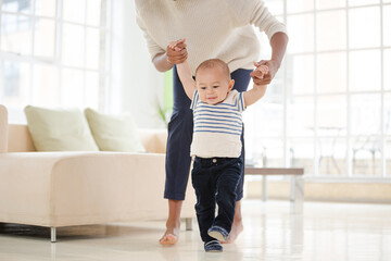 Mother helping baby boy walk in living room
