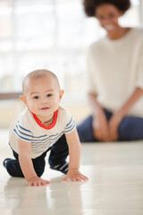 Mother watching baby boy crawl in living room