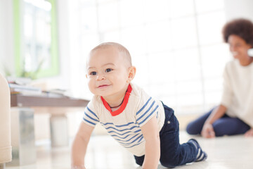 Mother watching baby boy crawl on floor