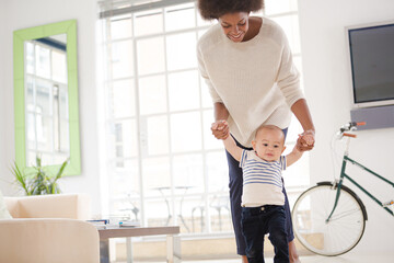 Mother helping baby boy walk on floor