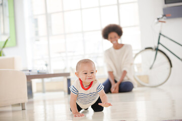 Mother watching baby boy crawl on floor