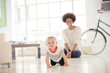 Mother watching baby boy crawl on floor