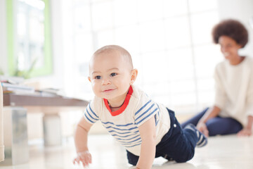 Mother watching baby boy crawl on floor