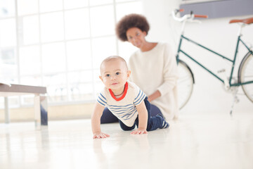 Mother watching baby boy crawl on floor