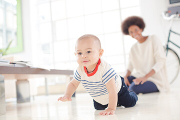Mother watching baby boy crawl on floor