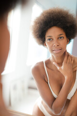 Woman in bra standing at bathroom mirror