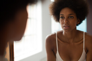 Serious woman in bra standing at mirror