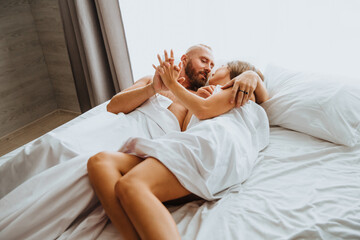 A loving couple hugs under the covers in bed in the bedroom at home. Early morning, lazy weekend,...