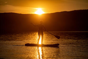 Girl on sup board with beautiful colored sunrise background mountains background