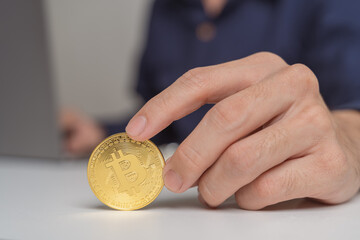 Close up hand of Businessman, trader, investor showing, holding gold Bitcoin Cryptocurrency, using computer laptop on white background at home. Young man trading, investing on Bitcoin Cryptocurrency.