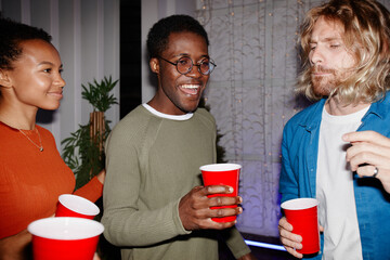Diverse group of young people enjoying house party indoors and holding red cups, shot with flash