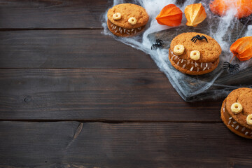 Cookies with cream paste in the shape of monsters for Halloween celebration. Funny homemade faces made of oatmeal cookies and boiled condensed milk. copy space