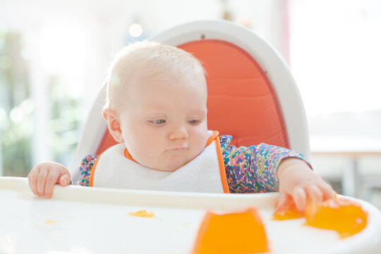 Baby girl playing with gelatin dessert in high chair