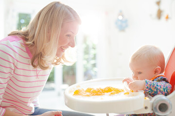 Mother feeding baby girl in high chair