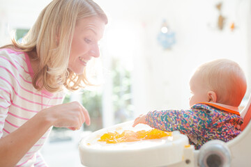 Mother feeding baby girl in high chair