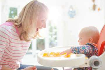 Mother feeding baby girl in high chair