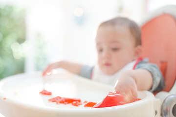 Baby boy eating gelatin dessert in high chair