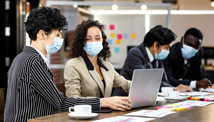 Multiracial smart formal businesspeople sitting face to face meeting and making group discussion at office, wearing face masks as new normal to protect or prevent virus in outbreak pandemic crisis.