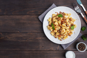 Stewed pasta with minced beef and vegetables, macaroni in Navy style on a plate. Dark wooden background. Copy space.