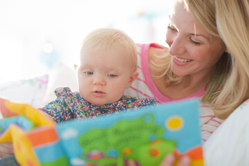 Obraz na płótnie Canvas Mother reading to baby girl on sofa