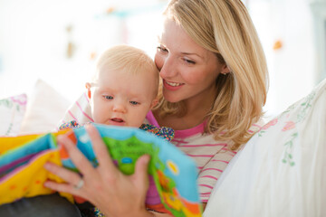 Mother reading to baby girl on sofa