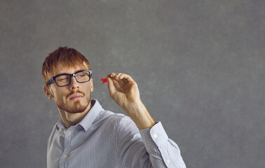 Close up portrait of a smart caucasian corporate worker aiming a dart at a target. Young guy in glasses and a shirt throws darts with a confident expression. Business concept and goal achievement.