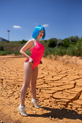 Beautiful young model girl with short blue hair and pink bathing suit  posing in the desert. Cracks in the sand 