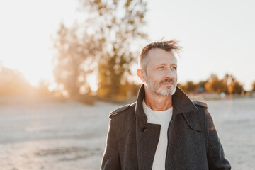 Lone senior man walking on a sandy beach at sunset