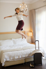 Businesswoman jumping on bed in hotel room